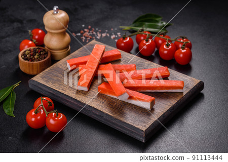 Crab sticks on a cutting Board with a knife. On black concrete background 91113444