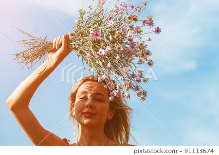 Young beautiful woman smiling to the sun holding a bouquet of wildflowers above her head 91113674