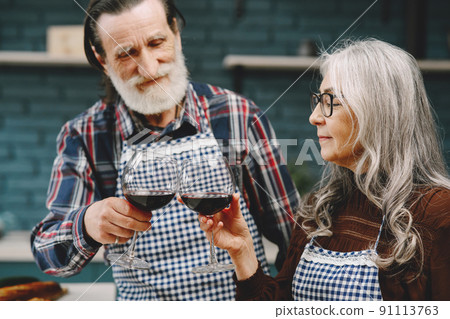 Couple senior caucasian husband and wife in casual dress. Standing in kitchen and tasting red wine. 91113763