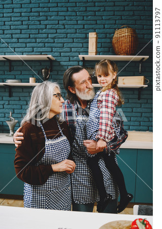 Mature couple and their granddaughter preparing food. Wearing aprons, modern kitchen interior. Mature couple and their granddaughter preparing food. Wearing aprons, modern kitchen interior. 91113797