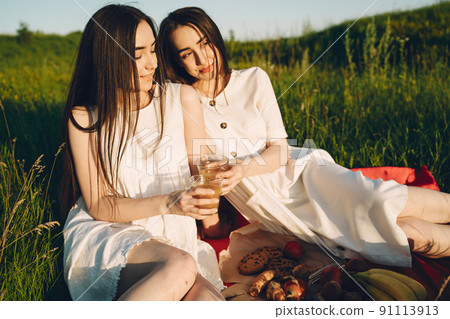 Two pretty sisters in a field of wheat. Beautiful two girls with long healthy hair enjoying nature on summer. Girls on a picnic. Two pretty sisters in a field of wheat. Beautiful two girls with long healthy hair enjoying nature on summer. Girls on a picnic. 91113913