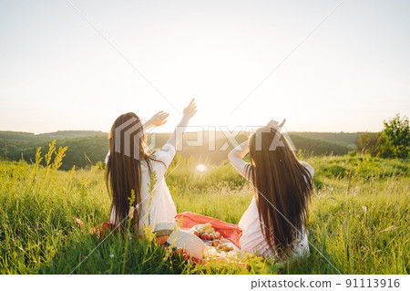 Two pretty sisters in a field of wheat. Beautiful two girls with long healthy hair enjoying nature on summer. Girls on a picnic. Two pretty sisters in a field of wheat. Beautiful two girls with long healthy hair enjoying nature on summer. Girls on a picnic. 91113916