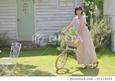Young woman riding a bicycle on the grass in the garden 91114028