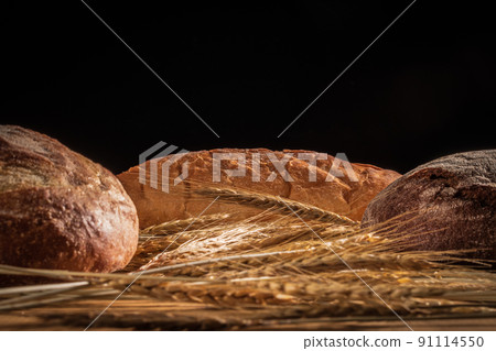 Three loaves of bread and ears of wheat on a black background 91114550