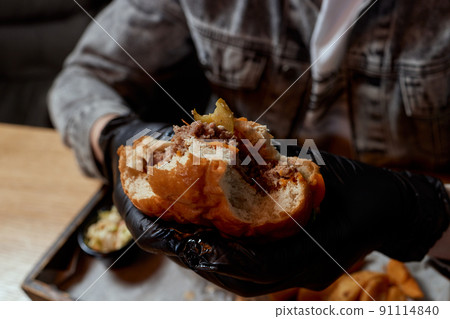 Man in black gloves eating beef burger. Closeup. 91114840