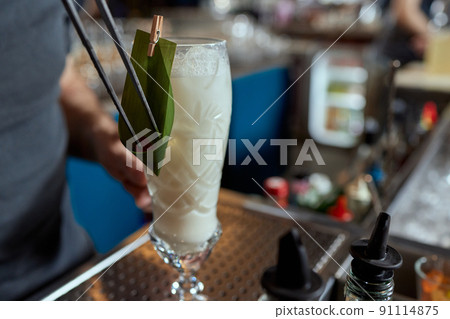 Barman in shirt and apron making an alcoholic drink with ice in a cocktail glass. 91114875