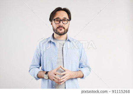 Portrait of thoughtful young Asian man in shirt and glasses standing against light gray background and touching tips of fingers while speculating about problem Portrait of thoughtful young Asian man in shirt and glasses standing against light gray background and touching tips of fingers while speculating about problem 91115268