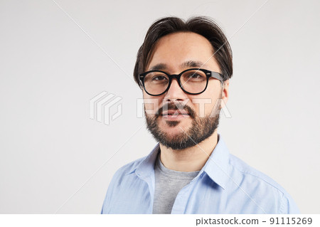 Portrait of content confident young Asian bearded man in glasses standing against light gray background Portrait of content confident young Asian bearded man in glasses standing against light gray background 91115269