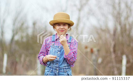 a funny little girl in a hat eats green onions and waves at the sharpness 91115337