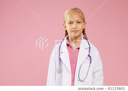 Content confident girl in lab coat wearing purple stethoscope around neck standing against pink background and looking at camera 91115601