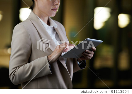 Close-up of contemporary businesswoman in jacket standing on night street and analyzing online file on tablet Close-up of contemporary businesswoman in jacket standing on night street and analyzing online file on tablet 91115904