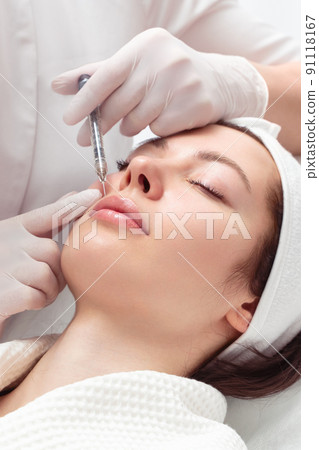 Lip augmentation and correction procedure in a cosmetology salon. The specialist makes an injection in the patient lips. 91118167