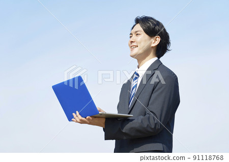 在藍天背景下使用筆記本電腦的商人 91118768