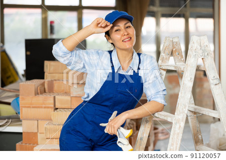 Portrait of a woman builder posing near a stepladder Portrait of a woman builder posing near a stepladder 91120057