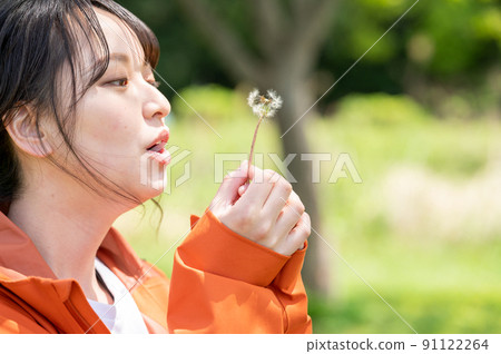 Young woman blowing dandelion fluff in the park Young woman blowing dandelion fluff in the park 91122264