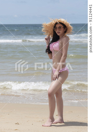 Girl in pinky bikini with hat relaxing and posing at beach Girl in pinky bikini with hat relaxing and posing at beach 91124441