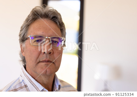 Close-up portrait of confident caucasian senior man wearing eyeglasses against wall in nursing home 91125334