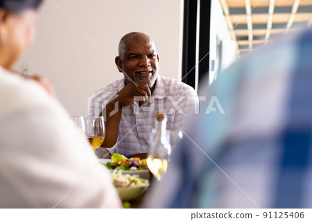 Smiling biracial senior man looking at friends while having lunch at dining table in nursing home Smiling biracial senior man looking at friends while having lunch at dining table in nursing home 91125406