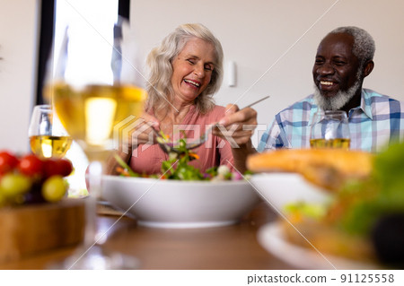 Low angle view of multiracial cheerful senior couple having lunch at dining table in nursing home Low angle view of multiracial cheerful senior couple having lunch at dining table in nursing home 91125558