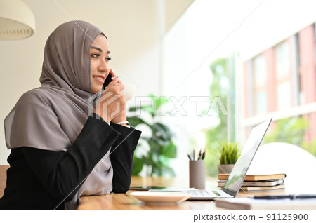 Gorgeous young asian muslim woman or businesswoman with hijab talking on the phone 91125900
