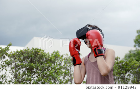 Young female wearing VR headset for working out boxing, aerobic training for boxing punch in virtual reality in simulation world. Young female wearing VR headset for working out boxing, aerobic training for boxing punch in virtual reality in simulation world. 91129942