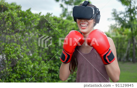 Young female wearing VR headset for working out boxing, aerobic training for boxing punch in virtual reality in simulation world. Young female wearing VR headset for working out boxing, aerobic training for boxing punch in virtual reality in simulation world. 91129945
