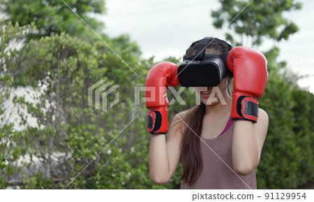 Young female wearing VR headset for working out boxing, aerobic training for boxing punch in virtual reality in simulation world. Young female wearing VR headset for working out boxing, aerobic training for boxing punch in virtual reality in simulation world. 91129954
