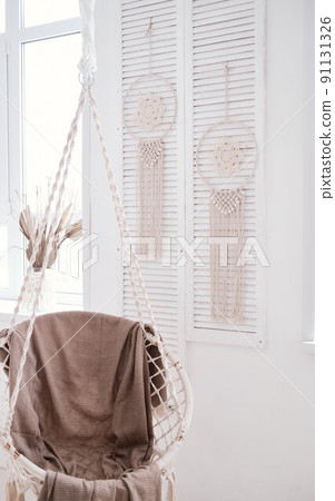 hanging knitted chair against the backdrop of dream catchers, in a white room. Boho style 91131326