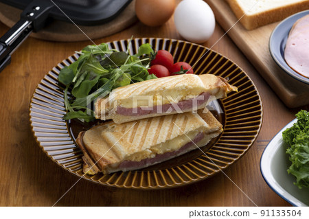 Make a hot sandwich with eggs, ham and cheese sandwiched between breads with a hot sandwich maker 91133504