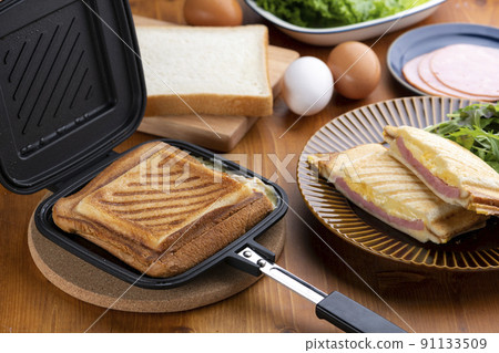 用熱三明治機製作一個熱三明治,將雞蛋、火腿和奶酪夾在麵包之間 用熱三明治機製作一個熱三明治,將雞蛋、火腿和奶酪夾在麵包之間 91133509
