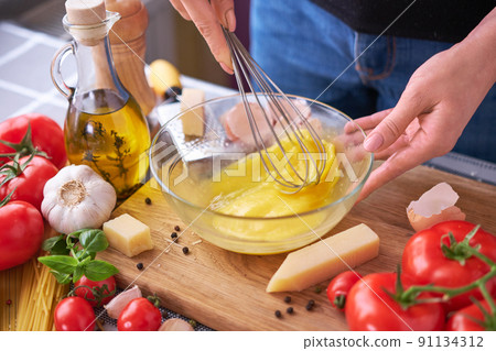 Woman beating egg yolks with a whisk making homemade pasta carbonara 91134312