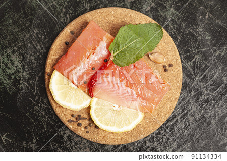 Pieces of lightly salted trout with herbs, spices and lemon on a wooden board top view 91134334