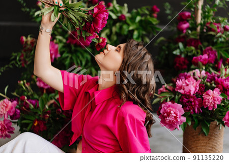 an attractive young woman in a pink blouse with peony flowers an attractive young woman in a pink blouse with peony flowers 91135220