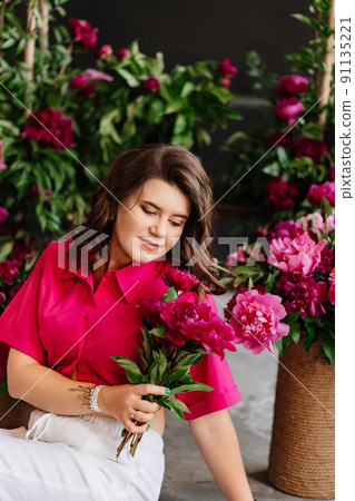 an attractive young woman in a pink blouse with peony flowers an attractive young woman in a pink blouse with peony flowers 91135221