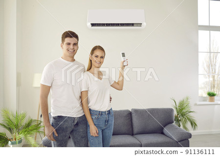 Happy couple enjoying using newly installed air conditioner in living room of their home. 91136111