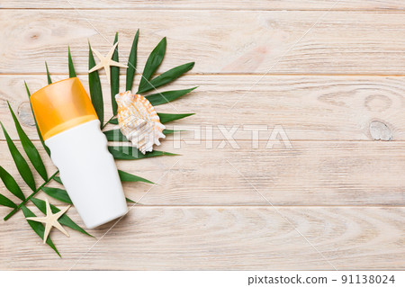 Sunscreen spray bottle. Bottle with sun protection cream and sea shells with tropical green leaf on color background, top view Sunscreen spray bottle. Bottle with sun protection cream and sea shells with tropical green leaf on color background, top view 91138024
