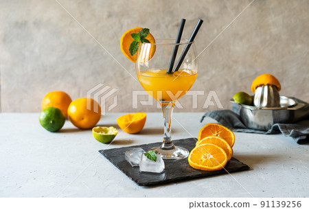 Yellow bird cocktail with rum, orange and lime juice, fruits, juicer, ice cubes, stone board on concrete background 91139256