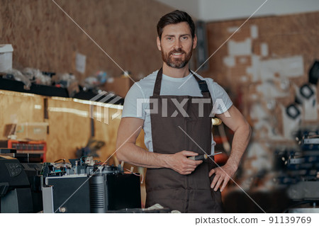 Repairman with a screwdriver standing on background of own workshop of coffee machines 91139769