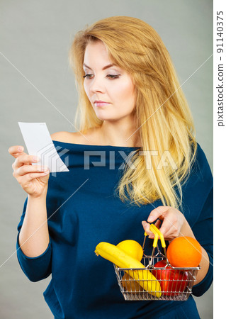 Worried woman holding shopping basket with fruits Worried woman holding shopping basket with fruits 91140375