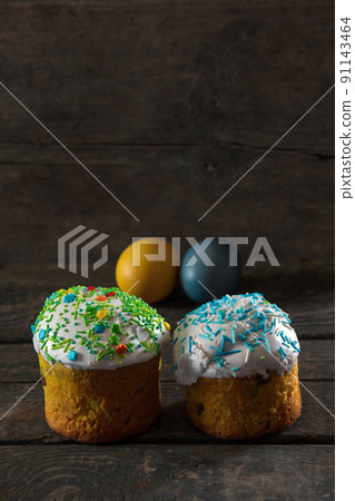 In the foreground there are 2 Easter cakes, in the back there are Painted eggs for Easter in the colors of the flag of Ukraine. Yellow and blue (cyan). On wood texture. Concept In the foreground there are 2 Easter cakes, in the back there are Painted eggs for Easter in the colors of the flag of Ukraine. Yellow and blue (cyan). On wood texture. Concept 91143464