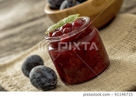 Home made plum jam in a jar and two plums next to it sitting on burlap sac 91146715