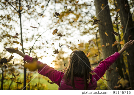 View from behind of a young woman standing in autumn woods with her arms outstretched 91146716