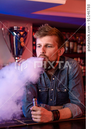 Vape. Vaping man in a cloud of vapor. Photo is taken in a vape bar. Vape. Vaping man in a cloud of vapor. Photo is taken in a vape bar. 91146788