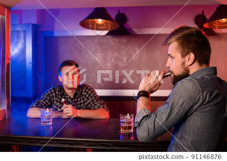 Two young men smoke electronic cigarettes in a vapebar 91146876