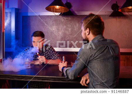 Vaping man holding a mod. A cloud of vapor at the vapebar. 91146887
