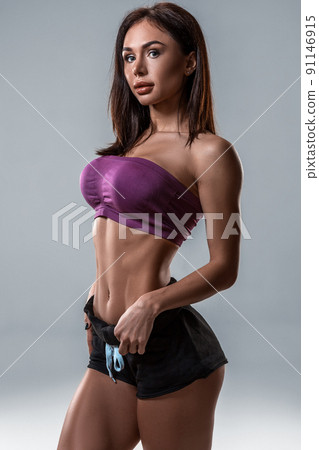 cropped close up body of fit woman wearing shorts and sport top showing slim beautiful stomach and abs in diet fitness and healthy lifestyle concept isolated on grey background 91146915