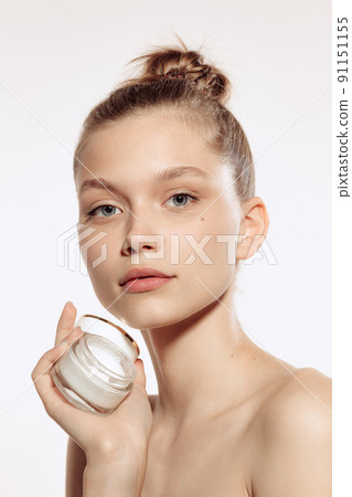 Half-length portrait of charming young girl without makeup holding cream bottle, posing isolated over white studio background. Half-length portrait of charming young girl without makeup holding cream bottle, posing isolated over white studio background. 91151155