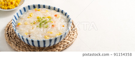 Delicious rice porridge congee with corn kernel and vegetables on white table background. Delicious rice porridge congee with corn kernel and vegetables on white table background. 91154358