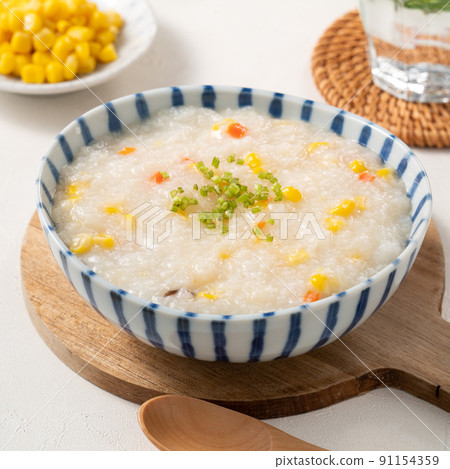 Delicious rice porridge congee with corn kernel and vegetables on white table background. Delicious rice porridge congee with corn kernel and vegetables on white table background. 91154359
