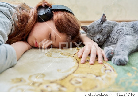 Preteen girl in headphones sleeping with cat on floor at home Preteen girl in headphones sleeping with cat on floor at home 91154710